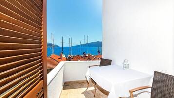 A balcony with a table and chairs, a view of the sea, and a wooden slatted wall.