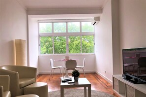 Ein Wohnzimmer mit Schlafsofa, Fernseher und Essecke mit Stühlen und Tisch.