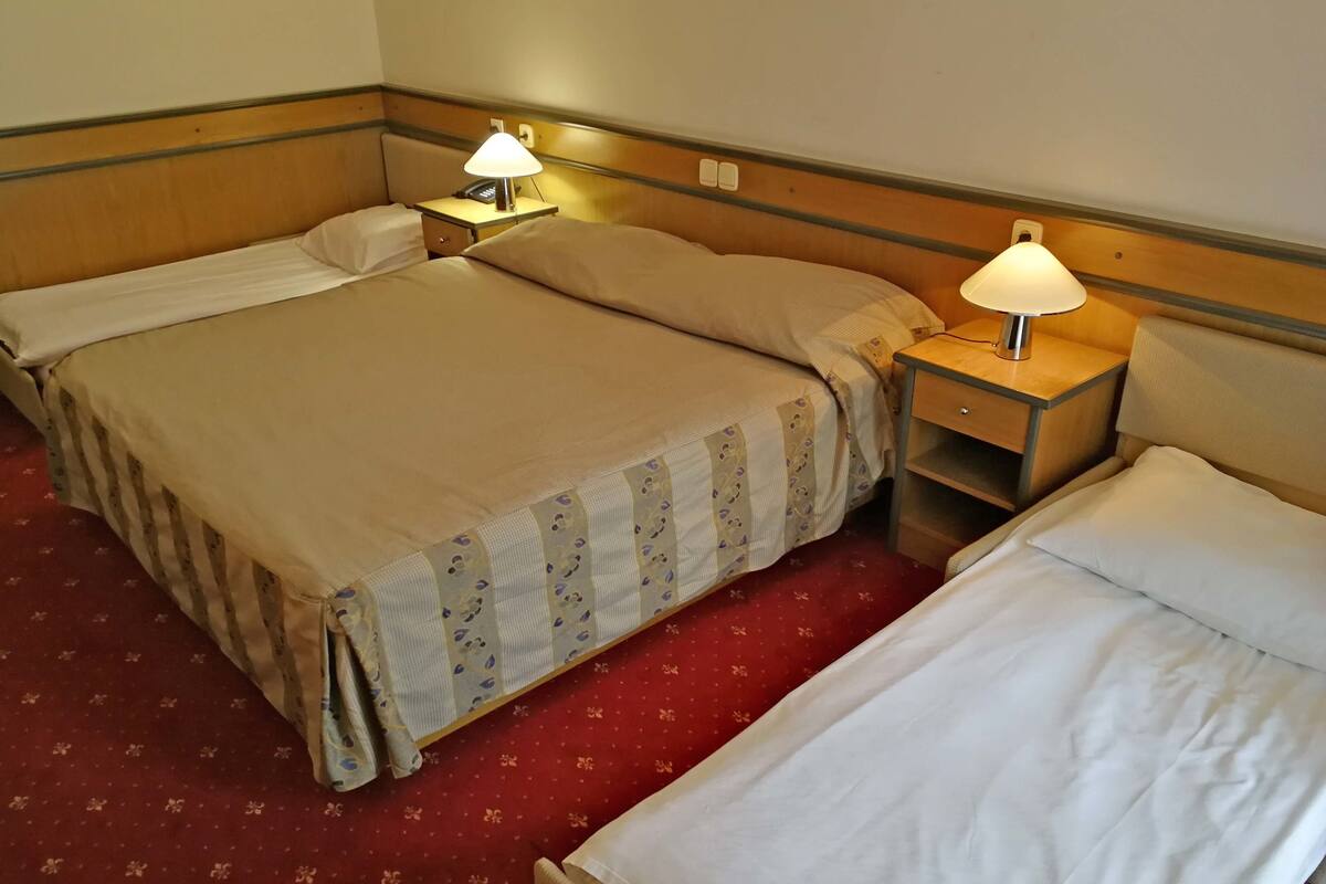 A hotel room with two beds, each with a pillow and a lamp on a bedside table.