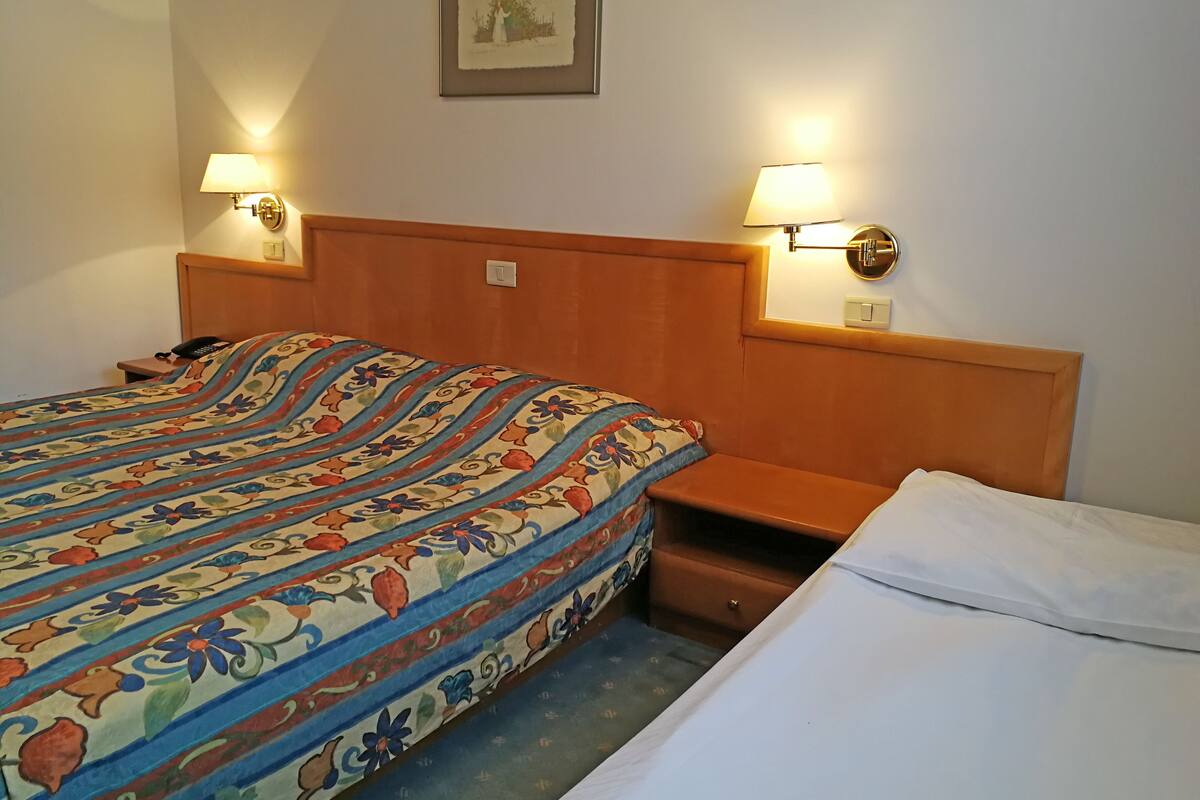 A hotel room with a large bed, two bedside lamps, a nightstand, and a small table.