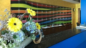 A reception area with a colorful striped wall, a wooden desk, and a floral arrangement. - Hotel Cerkno (Cerkno)