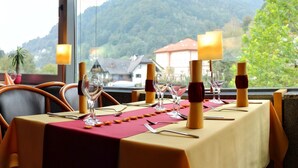 A dining table set with wine glasses, cutlery, and candles, with a mountain view through the window. - Hotel Cerkno (Cerkno)