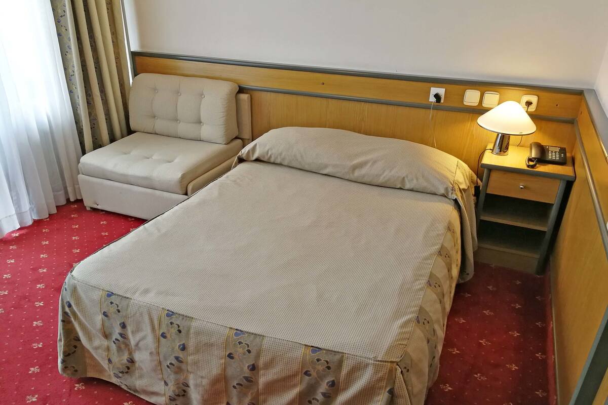 A hotel room with a bed, a small sofa, a nightstand with a lamp, and a telephone.