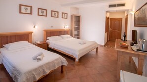 A hotel room with two beds, a desk with a chair, a bookshelf, and a door leading to another room. - Levantin Inn 1-3 Room sea side N10 (Sveti Stefan)