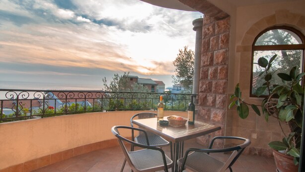 A balcony with a table and chairs, a bottle, and a basket of fruit. - Levantin Inn 1-3 Room sea side N10 (Sveti Stefan)