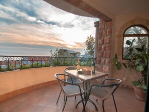 A balcony with a table and chairs, a bottle, and a basket of fruit.