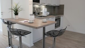 Eine moderne Küche mit einer Holz Arbeitsplatte, zwei Barhocker, einer Kaffeemaschine und einer Mikrowelle.
