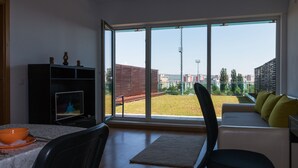 A modern living room with a large sliding glass door leading to a balcony, a dining area with a table and chairs, and a sofa with cushions. - AdrianApartments (Cluj-Napoca)