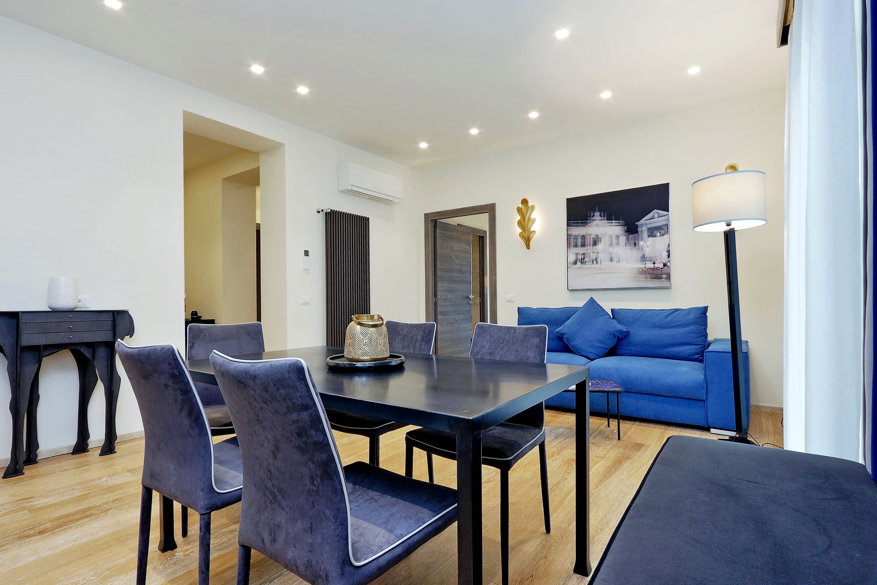 Ein modernes Wohnzimmer mit Essbereich, ausgestattet mit einem blauen Sofa, einem Esstisch mit Stühlen und einer Stehlampe.