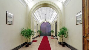 A hallway with a red carpet, potted plants, and framed pictures on the walls. - Luxurious three-room apartment with balcony, at the corner of Via Veneto (Roma)