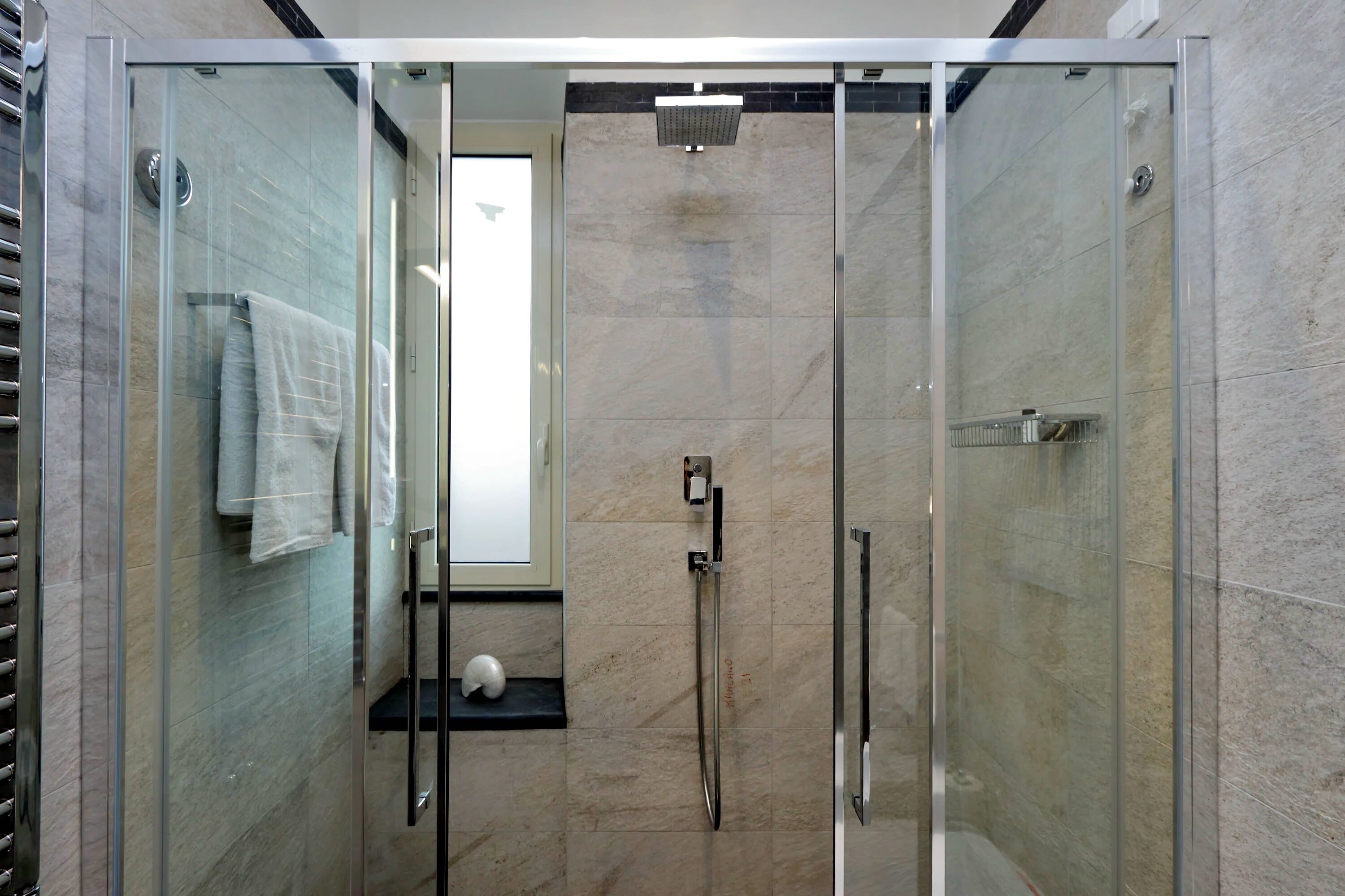 A modern shower area with glass doors, a handheld showerhead, and a towel rack.