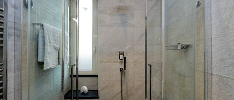A modern shower area with glass doors, a handheld showerhead, and a towel rack.