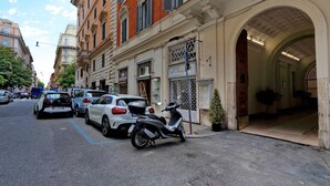 A street view with parked cars and a scooter, buildings with classical architecture, and a clear sky. - Luxurious three-room apartment with balcony, at the corner of Via Veneto (Roma)