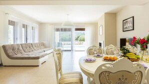 A spacious living area with a sofa, dining table set for four, and a view through the glass doors. - Eudora Luxury Stone Villa (Apokoronas)