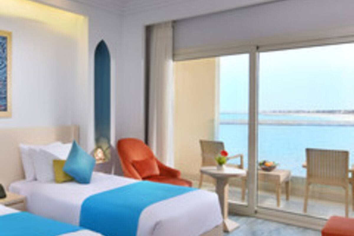 A hotel room with two beds, a balcony with a view of the sea, and a small table with a chair.
