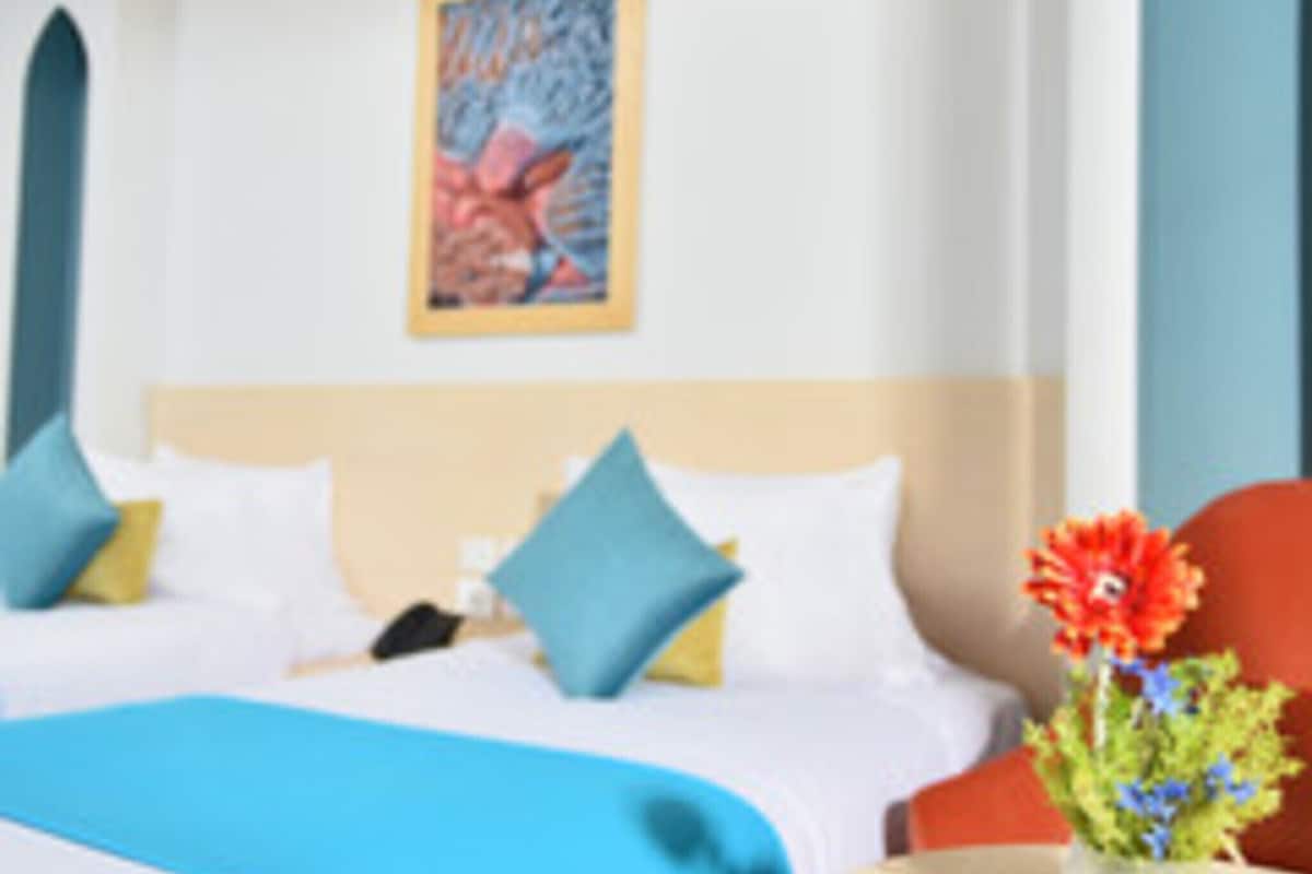 A hotel room with a bed, pillows, a vase with flowers, and a painting on the wall.