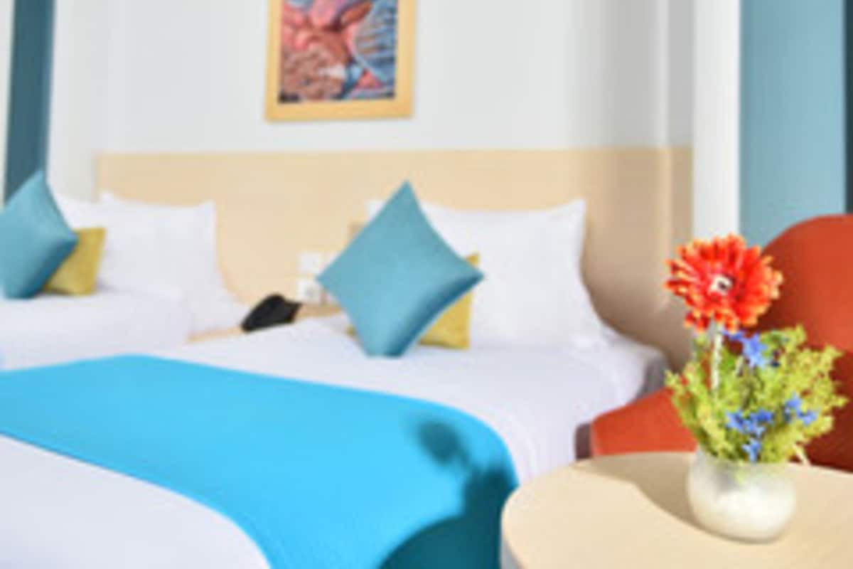 Une chambre d’hôtel avec un lit, des oreillers, un vase de fleurs et un tableau au mur.