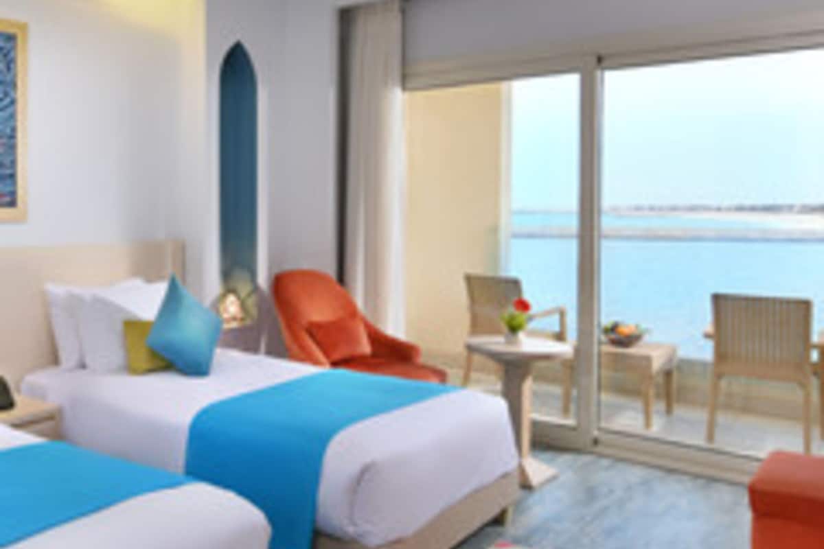 Une chambre d’hôtel avec deux lits, un balcon donnant sur la mer et une petite table avec une chaise.