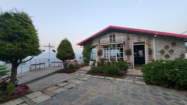 A building with a red roof, brick walls, and a balcony. There are potted plants and flowers in front of the building. - Viewtoria Resort (Dhanaulti)
