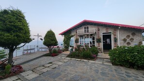 A building with a red roof, brick walls, and a balcony. There are potted plants and flowers in front of the building. - Viewtoria Resort (Dhanaulti)