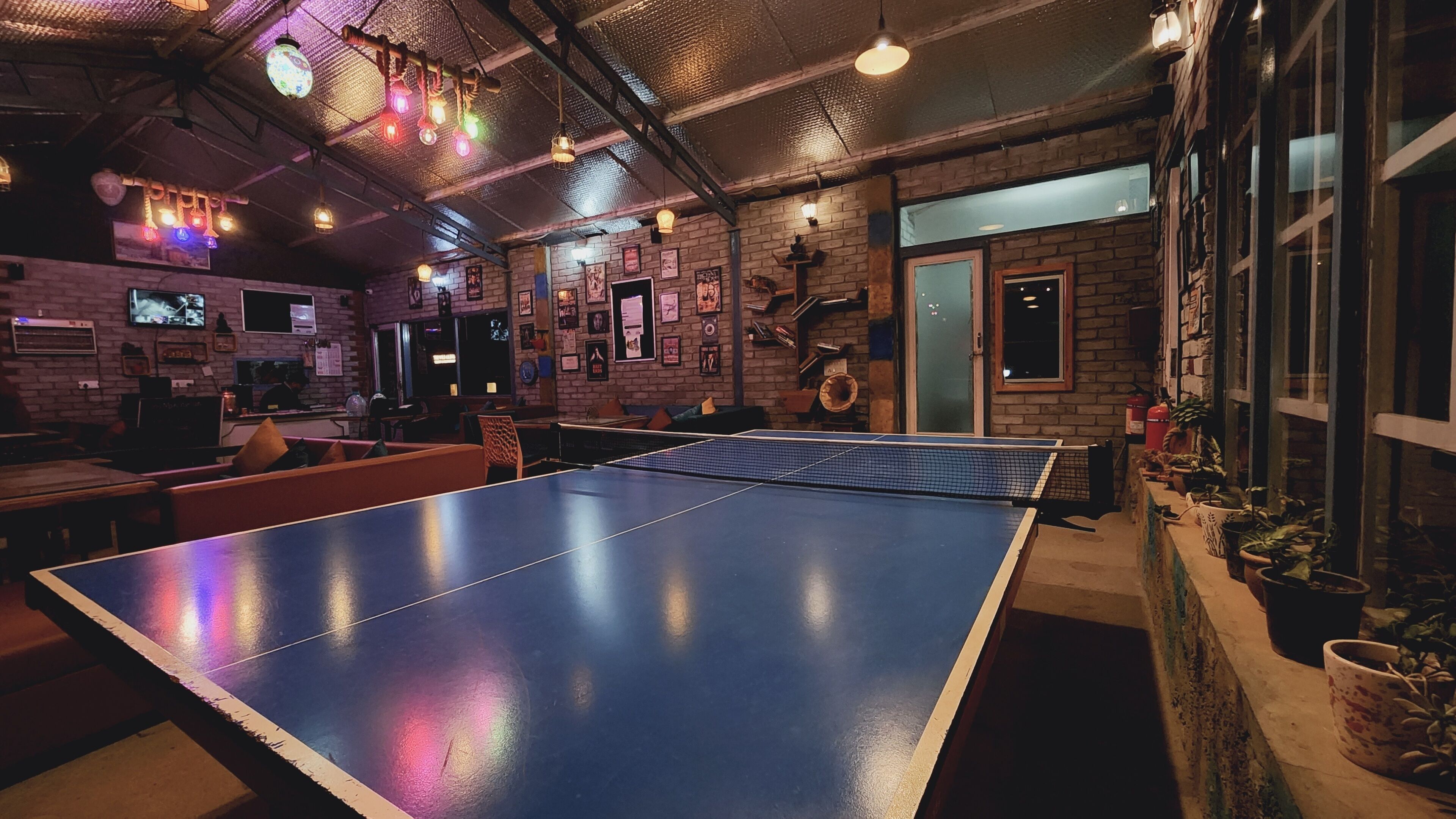 Une pièce avec une table de ping-pong, des murs en briques et diverses décorations, notamment des tableaux encadrés et un téléviseur.