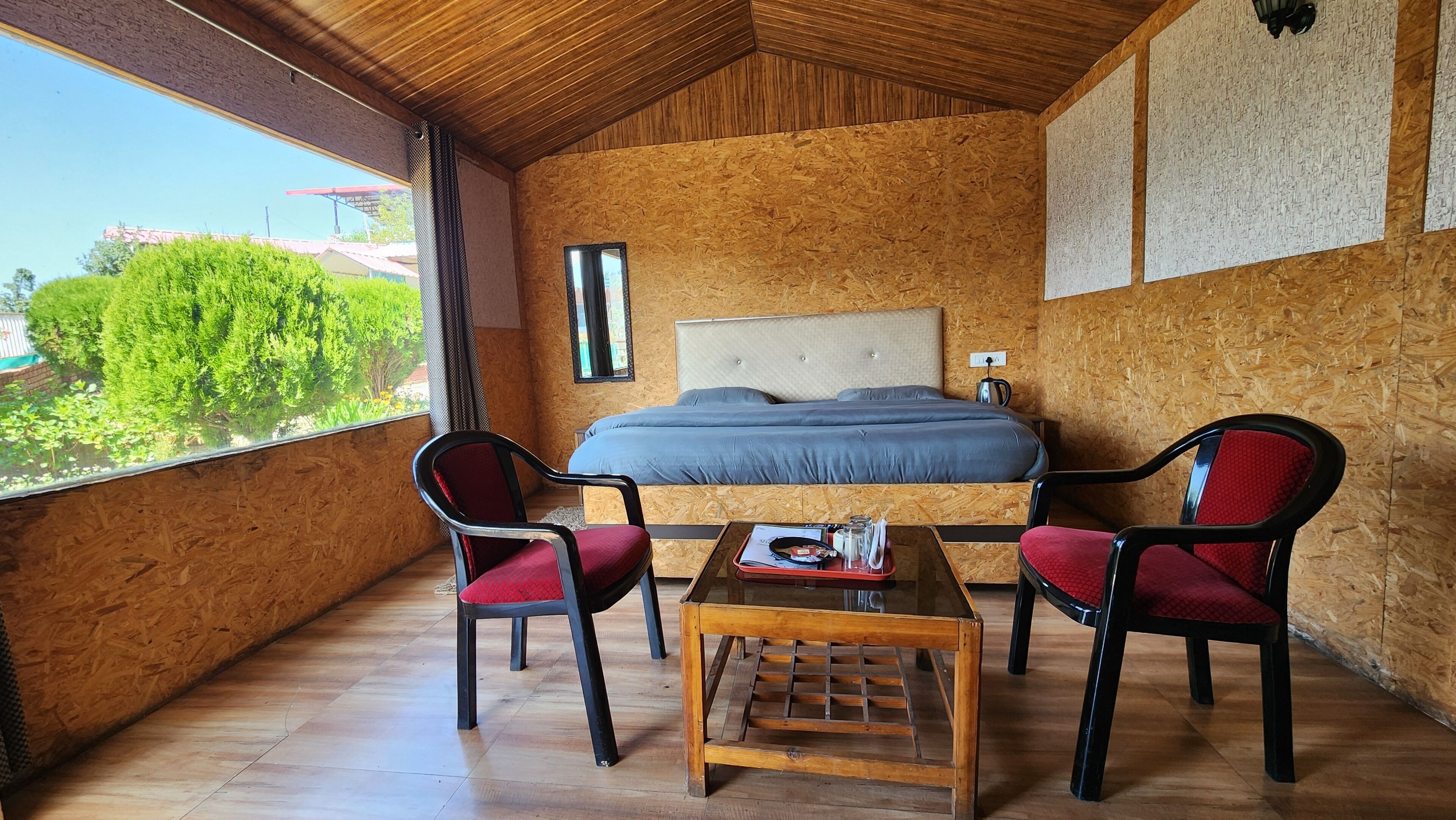 A bedroom with a large bed, two chairs, a small table, and a view of greenery outside.