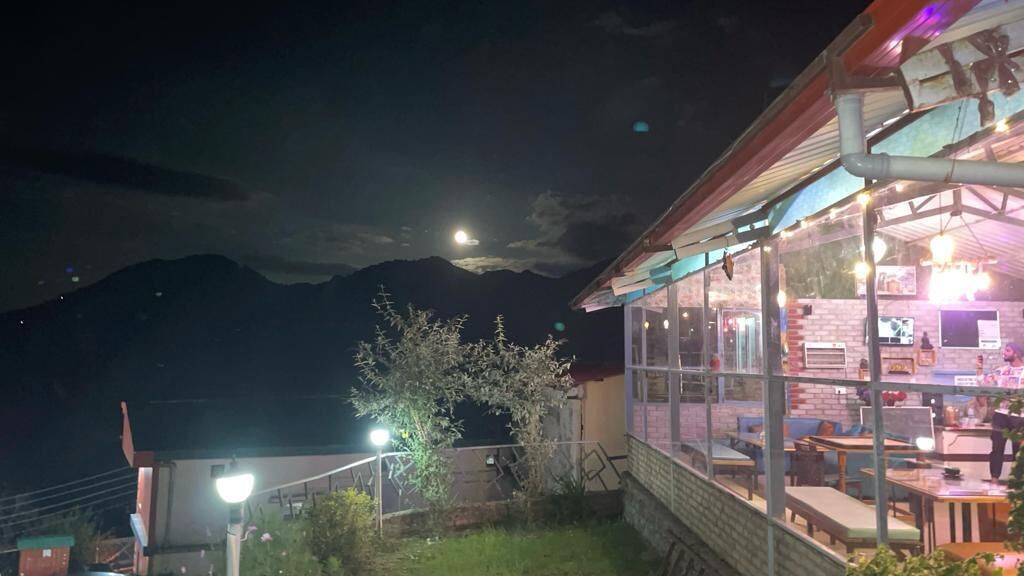 Un restaurant doté d’une terrasse, offrant une vue sur la montagne, et dont le bâtiment, partiellement visible, se distingue par son toit en pente.