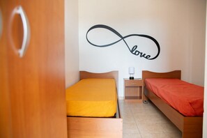 A bedroom with two beds, a nightstand, and a wall with a 'love' infinity symbol. - GuestHost - Cosy 100 sqm apartment, organized on two levels (ground and first floor), perfect for 5 people located 500m far from the sea and the beautiful beaches, has a large balcony with outdoor table, perfect for lunch and breakfast outside enjoying t (Santa Maria del Focallo)