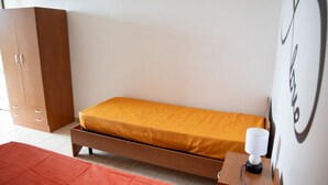A single bed with a wooden frame and a mattress, a wooden wardrobe, a bedside table with a lamp, and a red rug. - GuestHost - Cosy 100 sqm apartment, organized on two levels (ground and first floor), perfect for 5 people located 500m far from the sea and the beautiful beaches, has a large balcony with outdoor table, perfect for lunch and breakfast outside enjoying t (Santa Maria del Focallo)