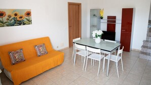 A living room with a sofa, a glass-top dining table, and a TV. - GuestHost - Cosy 100 sqm apartment, organized on two levels (ground and first floor), perfect for 5 people located 500m far from the sea and the beautiful beaches, has a large balcony with outdoor table, perfect for lunch and breakfast outside enjoying t (Santa Maria del Focallo)
