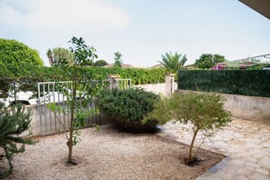 A landscaped garden with a gravel path, a metal gate, and various shrubs. - GuestHost - Cosy 100 sqm apartment, organized on two levels (ground and first floor), perfect for 5 people located 500m far from the sea and the beautiful beaches, has a large balcony with outdoor table, perfect for lunch and breakfast outside enjoying t (Santa Maria del Focallo)