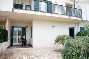 Ein zweistöckiges Gebäude mit Balkon, einer Tür mit Fensterläden und einer kleinen Außen-Sitzgelegenheit.