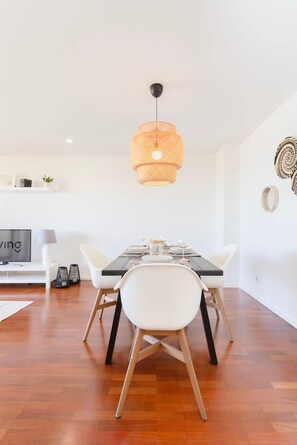 A modern dining area with a wooden floor, white chairs, a black table, and a woven pendant light.