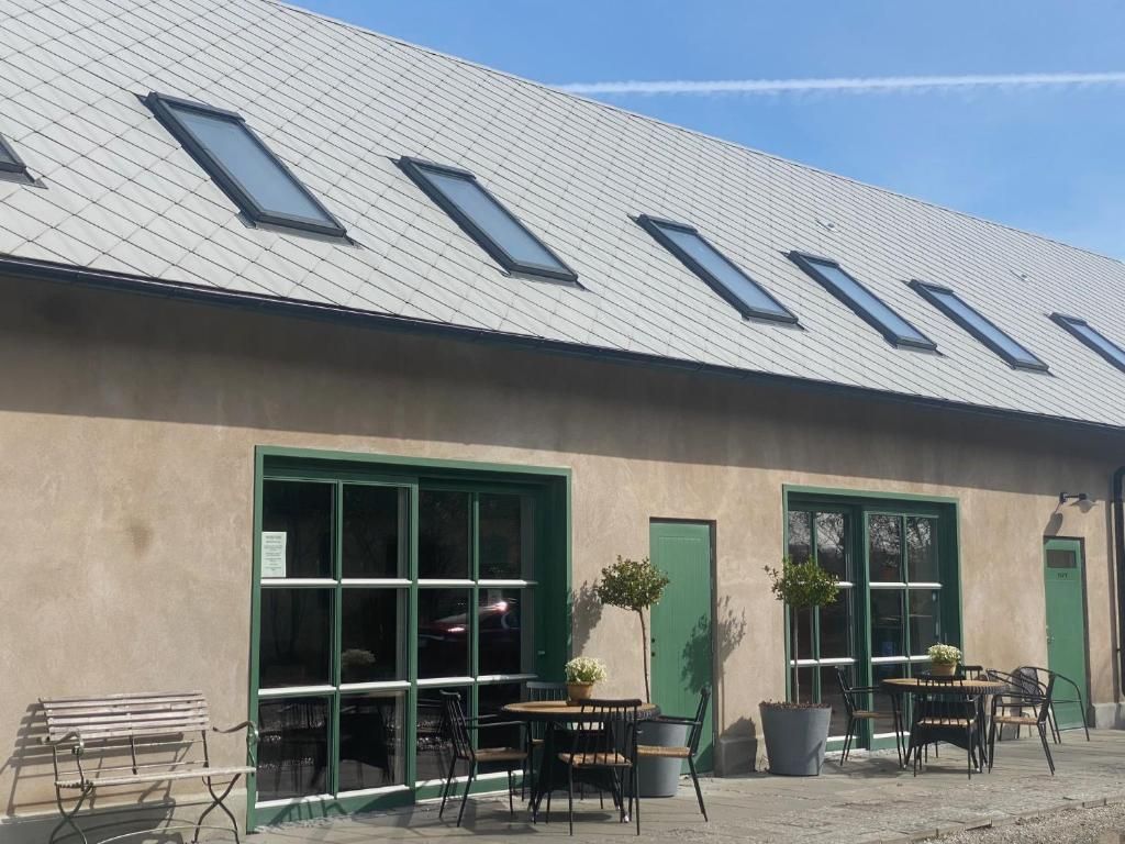 Un edificio con tetto spiovente, ampie finestre e area esterna con tavoli e sedie.