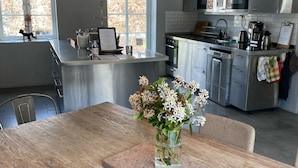 Una cocina moderna con electrodomésticos de acero inoxidable, un comedor con mesa de madera y un jarrón de flores sobre la mesa.