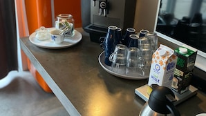 Una estación de café con una máquina de café, leche en envases y tazas sobre una encimera.