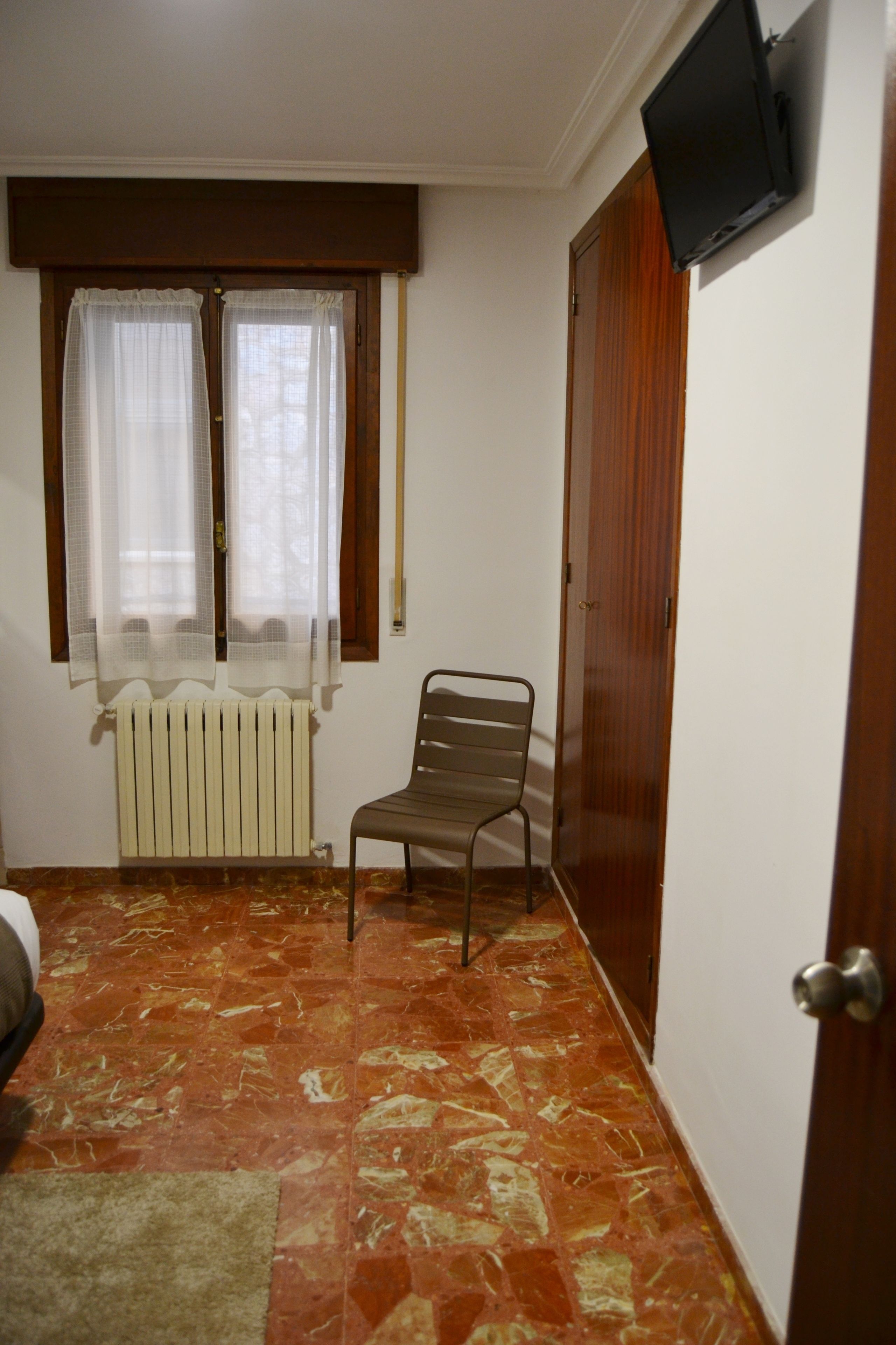 A room with a radiator, a chair, a wooden door, and a television mounted on the wall.
