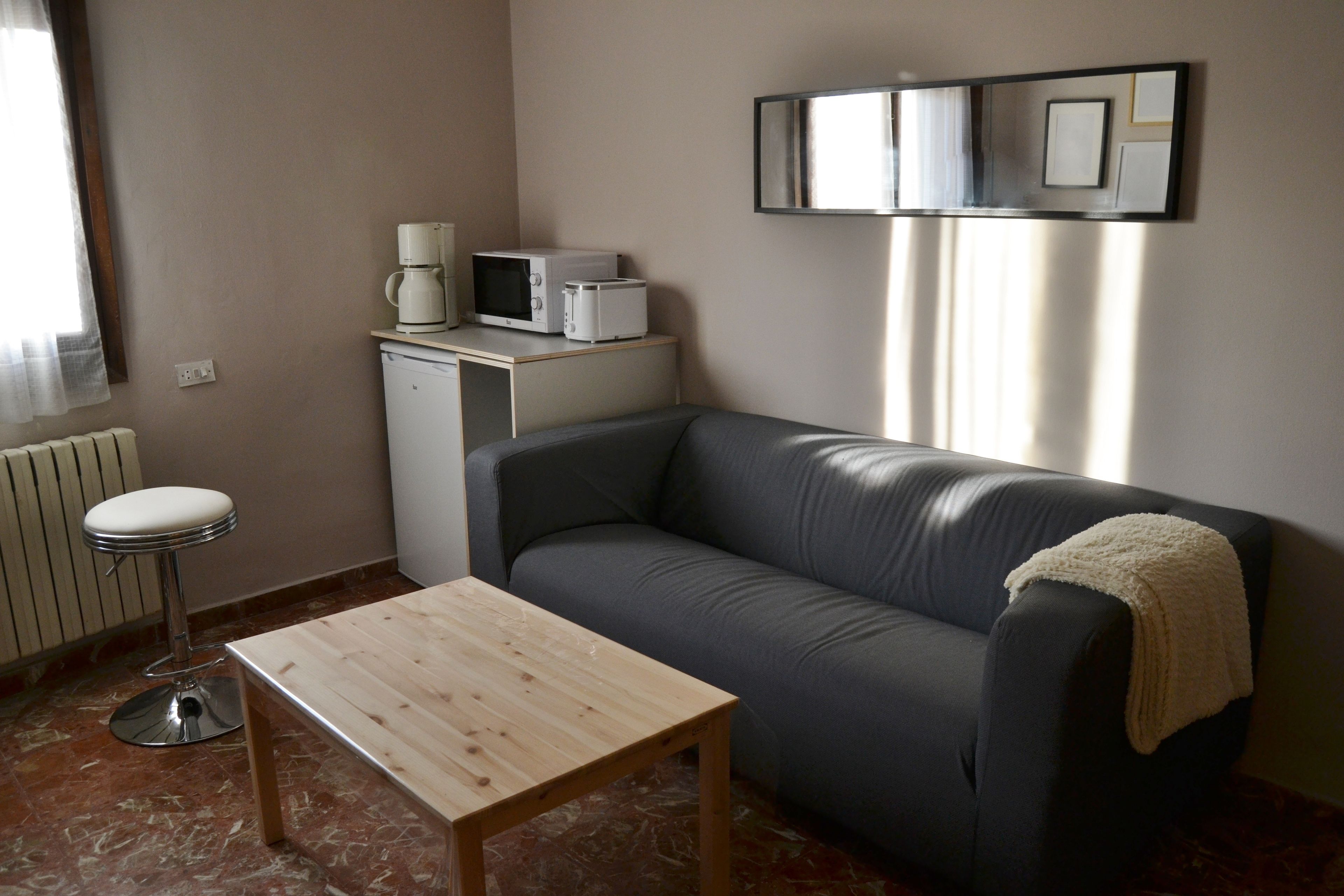 Una sala pequeña con sofá, una mesita de centro, una kitchenette con microondas y tostadora, y un radiador.