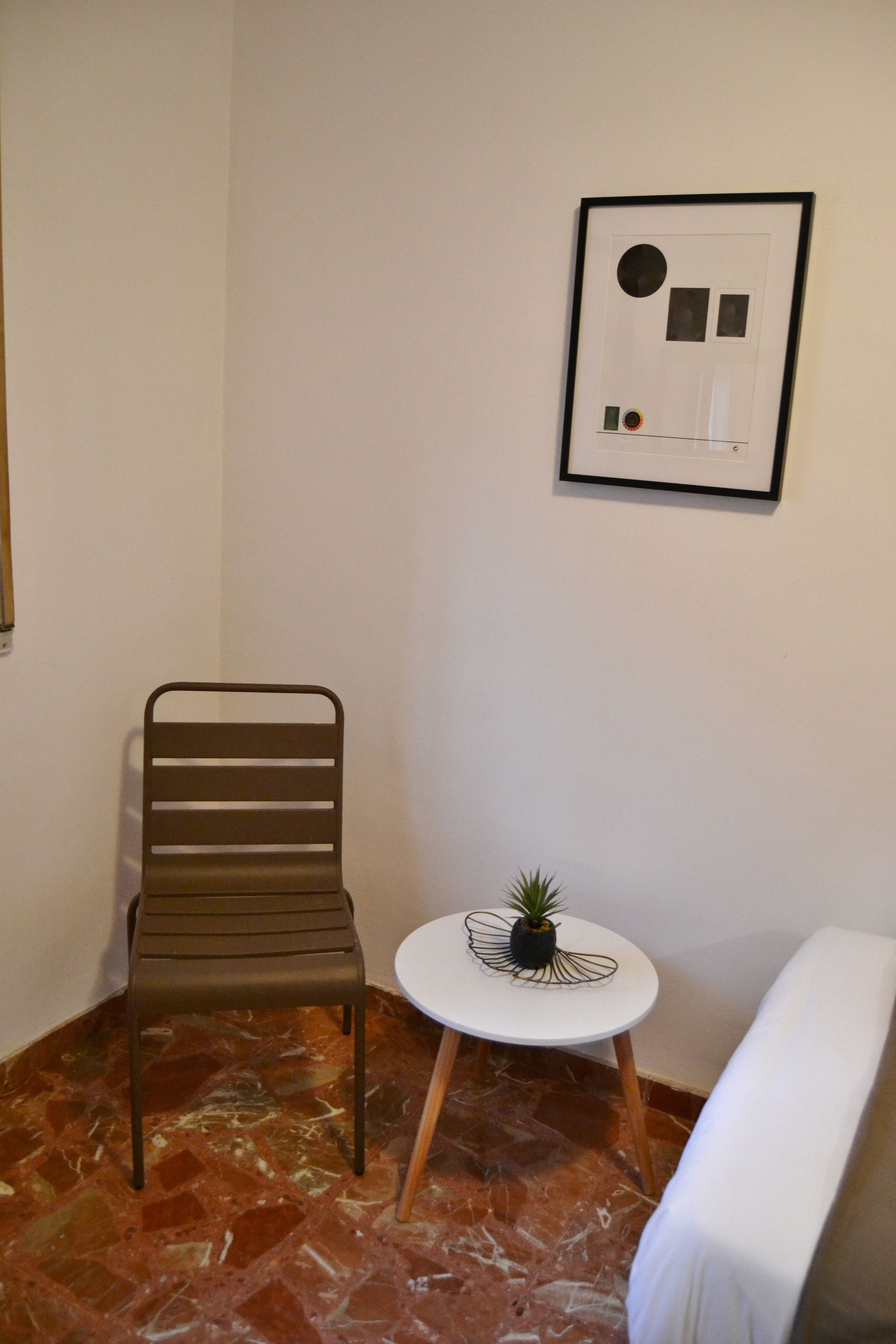 A small room with a metal chair, a round table with a plant, and a white sofa.