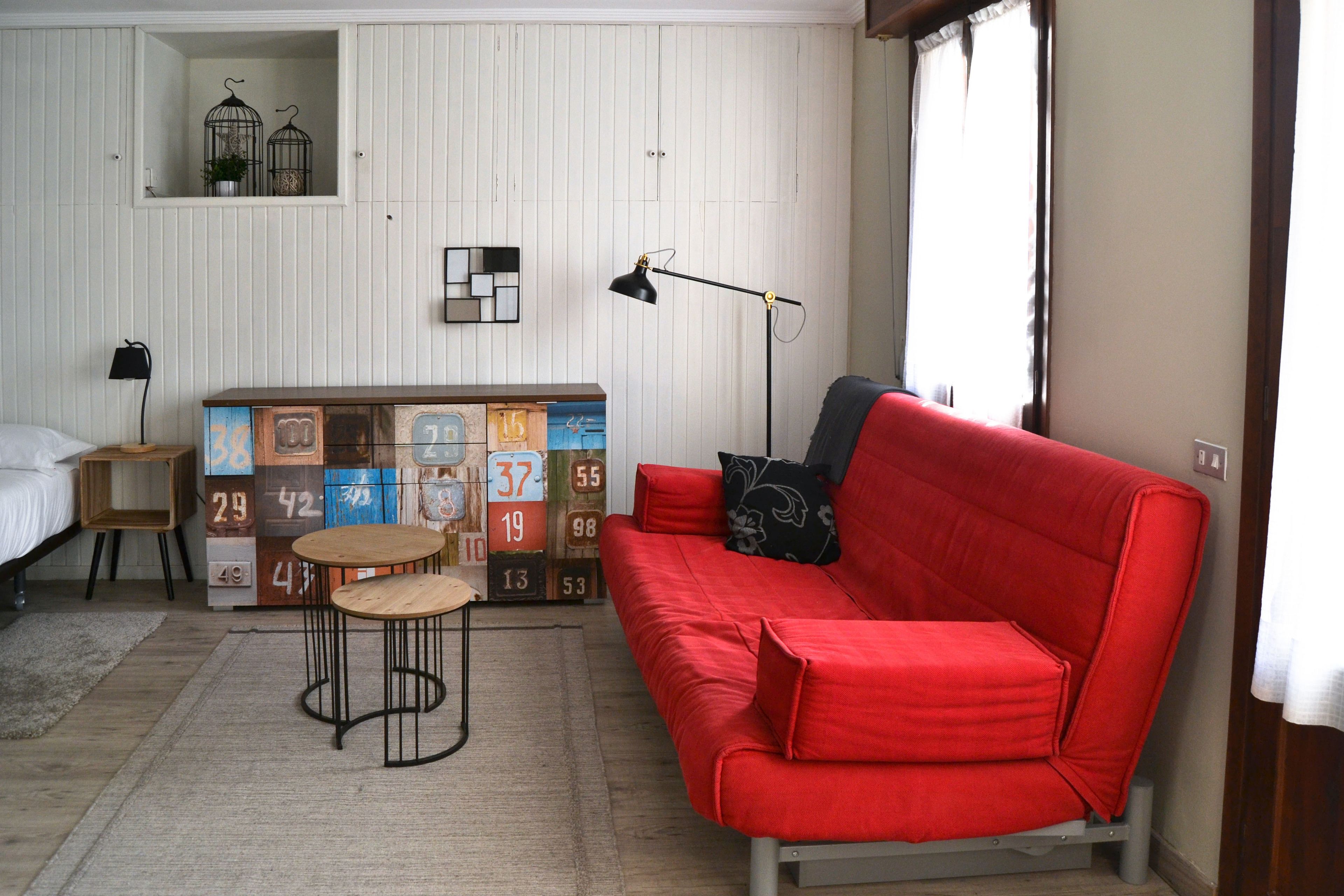 Una habitación con un sofá rojo, una mesita redonda pequeña, una lámpara, una cama y una pared con bloques numerados.