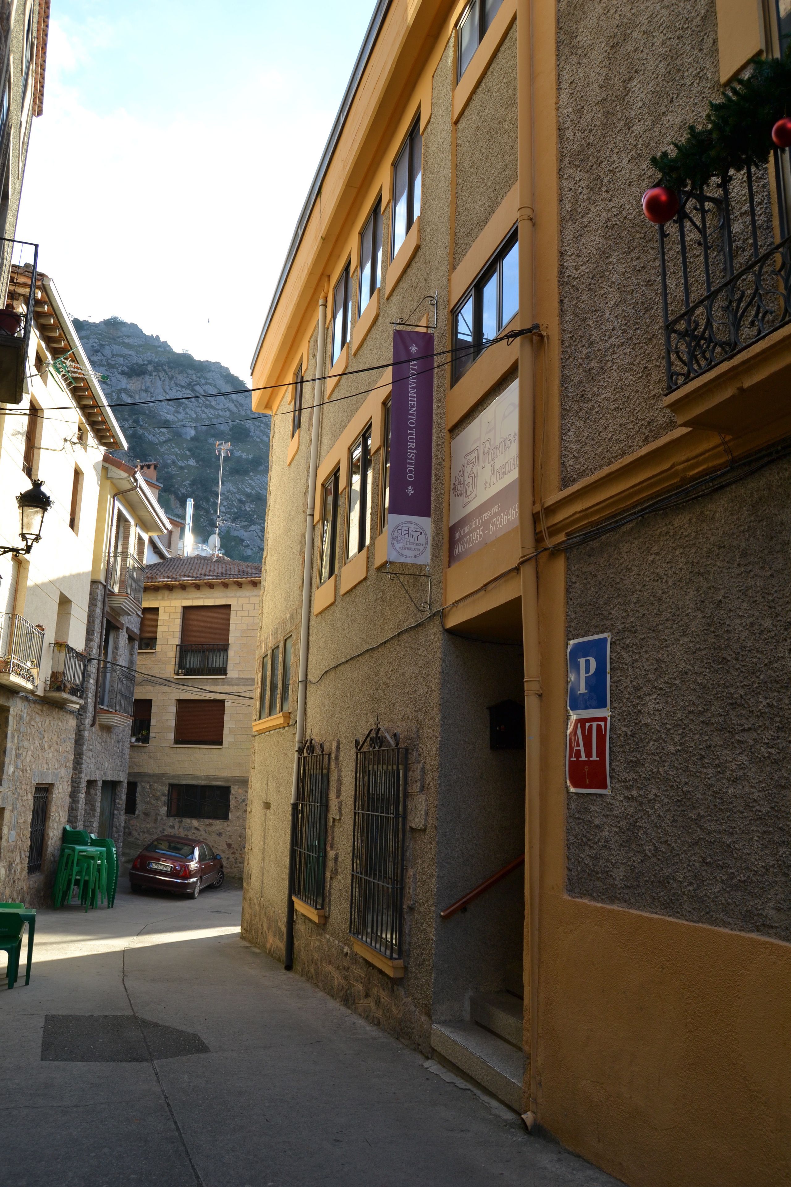 A narrow street with buildings on either side, a parked car, and a mountain in the background.