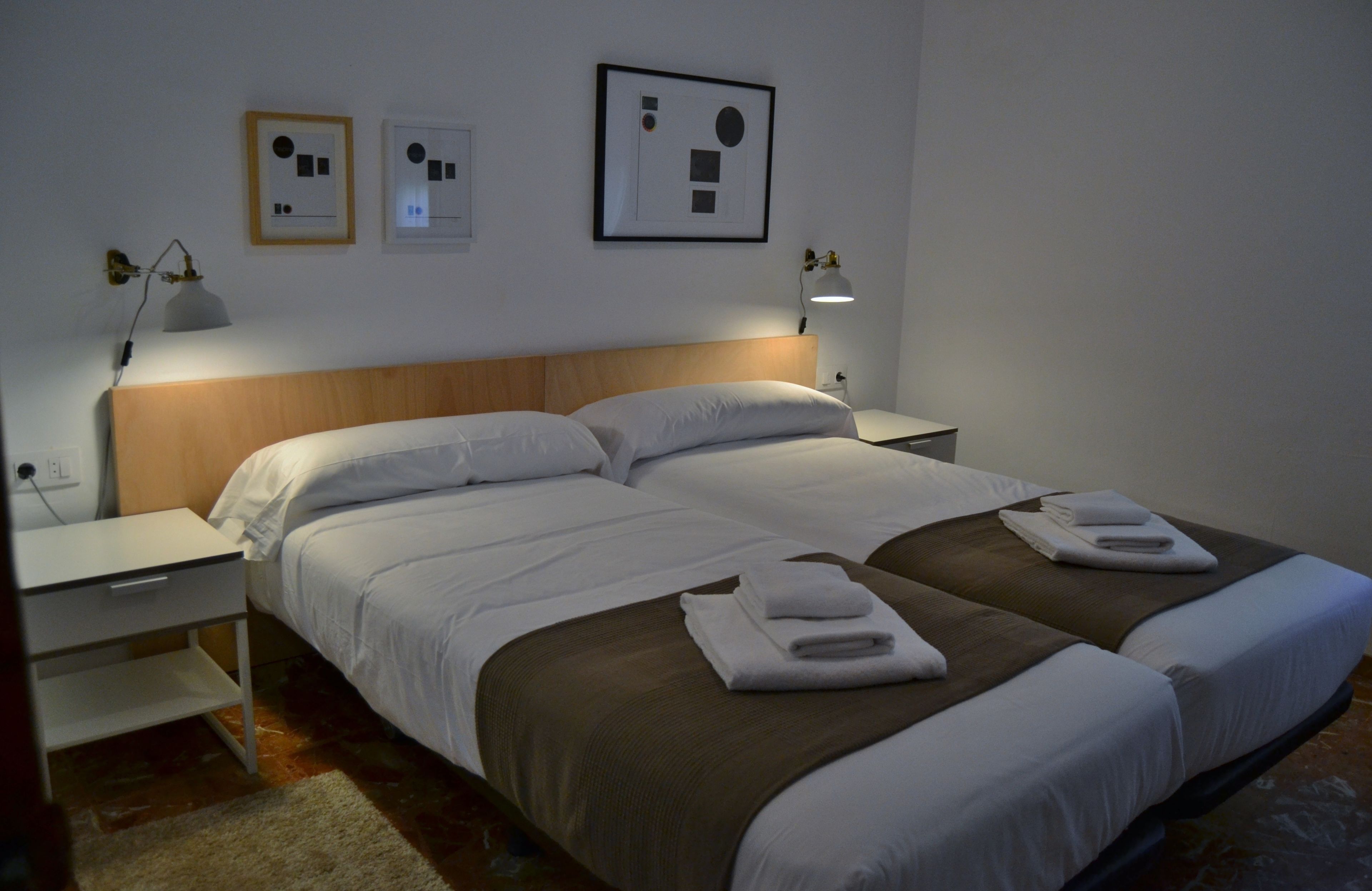 A hotel room with two beds, a wooden headboard, bedside tables with lamps, and artwork on the walls.
