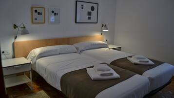 A hotel room with two beds, a wooden headboard, bedside tables with lamps, and artwork on the walls.