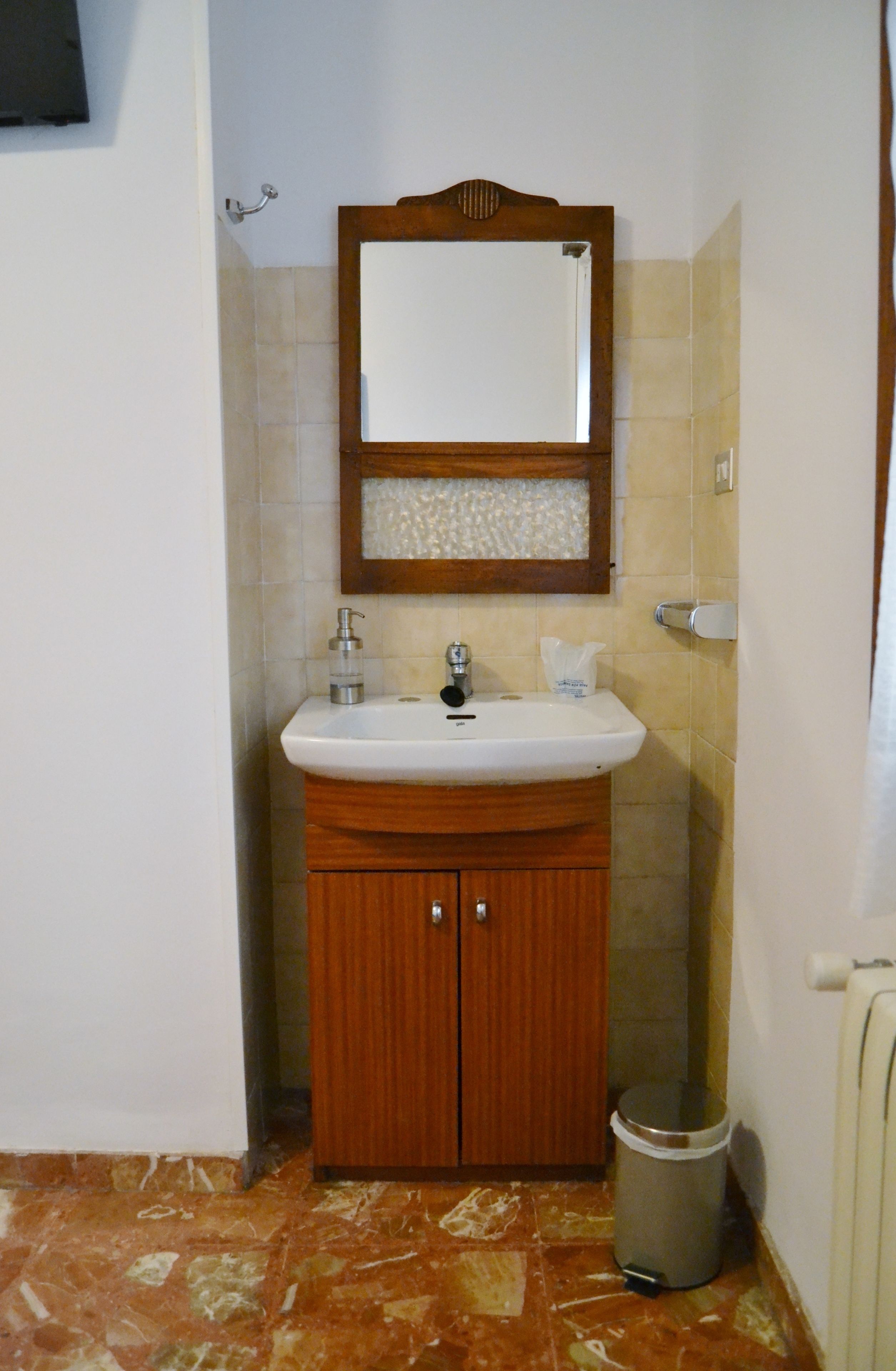 A bathroom with a wooden vanity, a white sink, a mirror, and a trash can.
