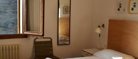 Quarto de hotel com cama, cadeira, mesa de cabeceira, luminária, espelho e janela.