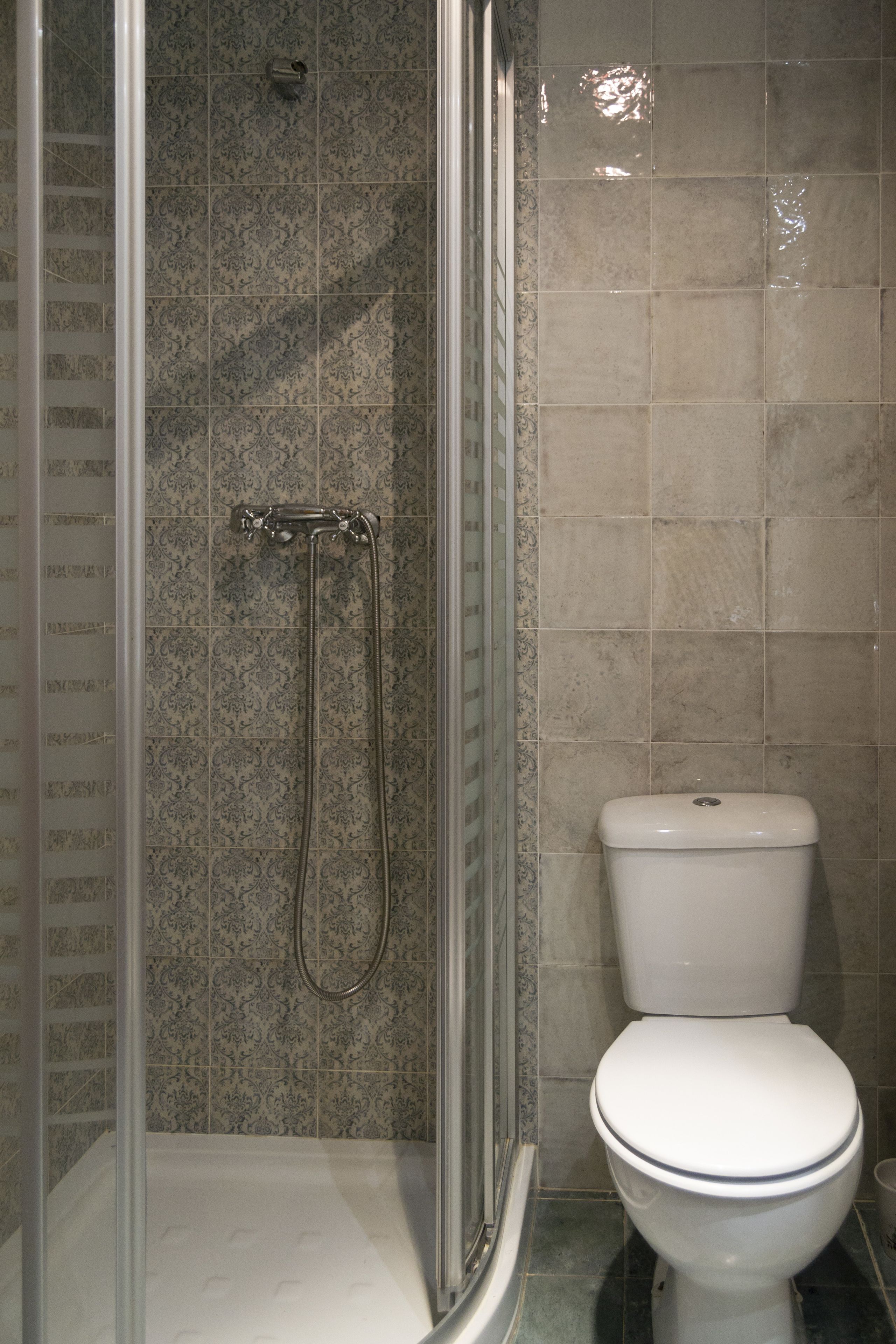 Baño con cabina de ducha, inodoro y azulejos estampados.