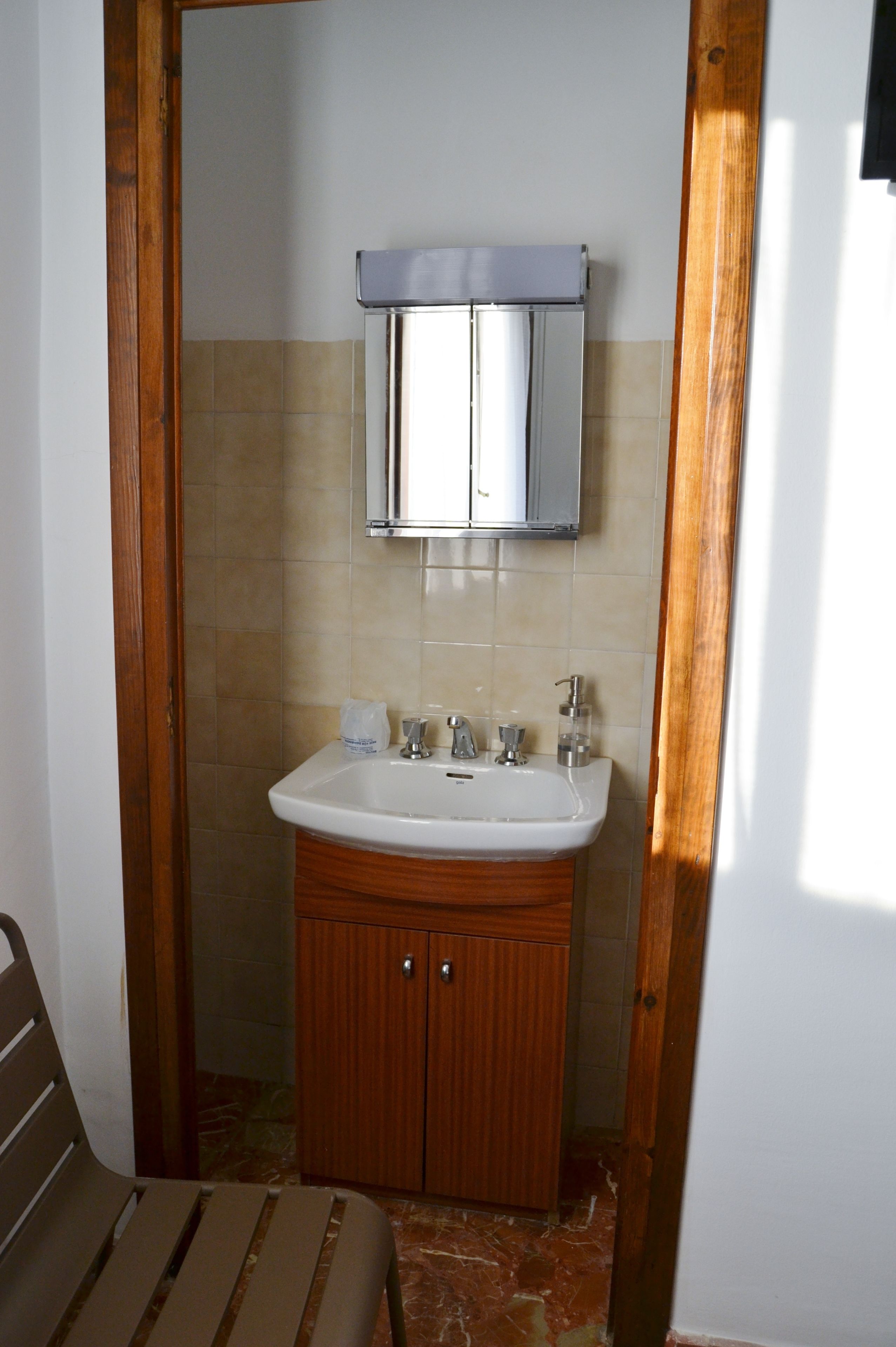 Un baño con un armario de madera, un lavamanos blanco y un espejo encima.