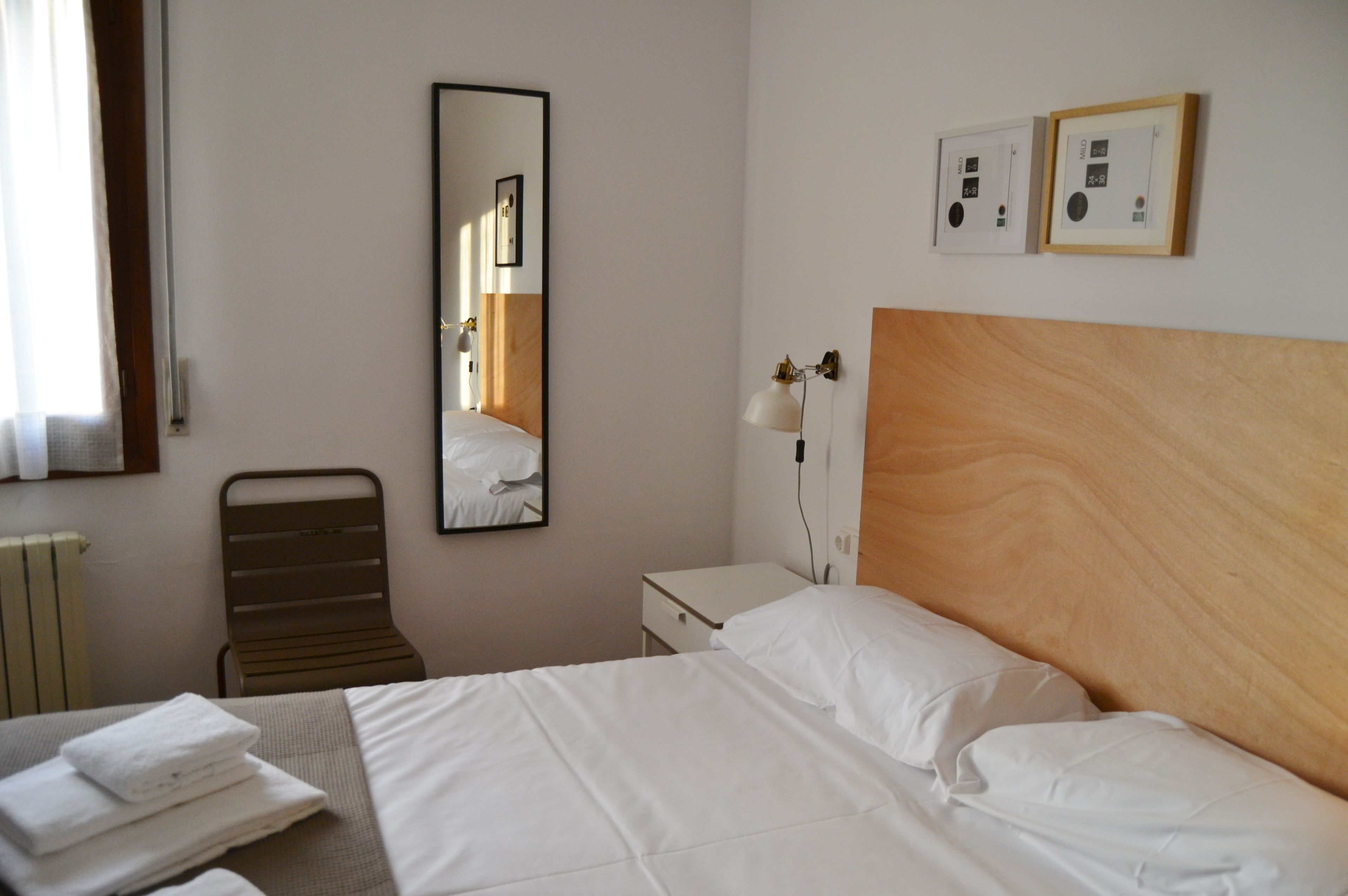 A hotel room with a bed, a chair, a nightstand, a lamp, and a mirror.