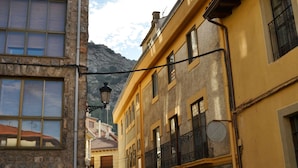 A narrow street with stone and yellow buildings, a mountain in the background, and a street lamp. - Tres Puentes Anguiano (Anguiano)