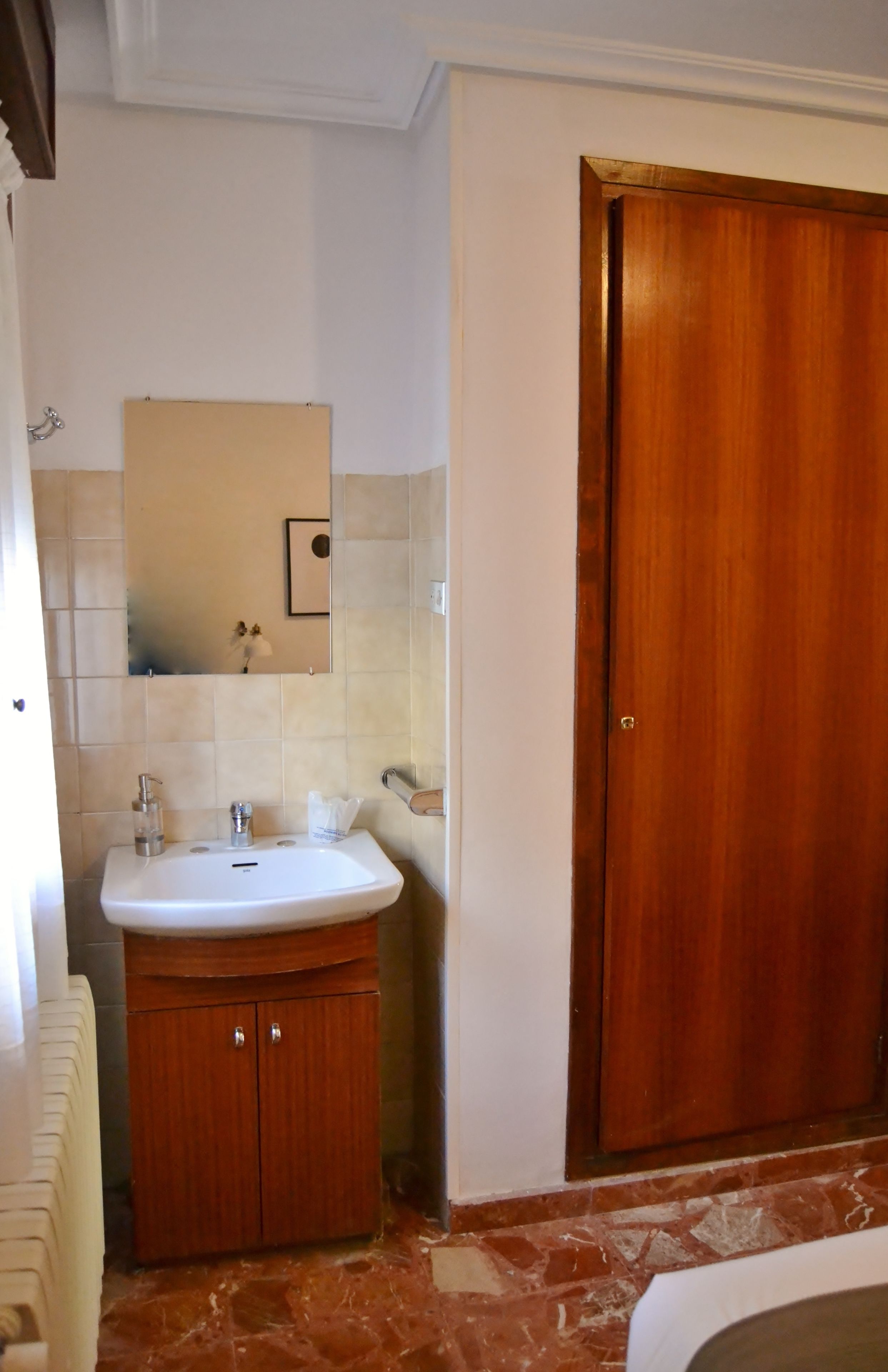 Un baño con lavamanos blanco, mueble de madera y puerta de madera.